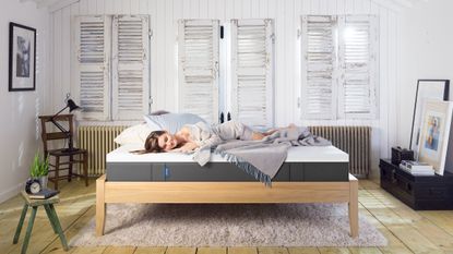 a woman sleeping on the Emma mattress in a rustic bedroom with wooden floor and blinds Emma mattress deals