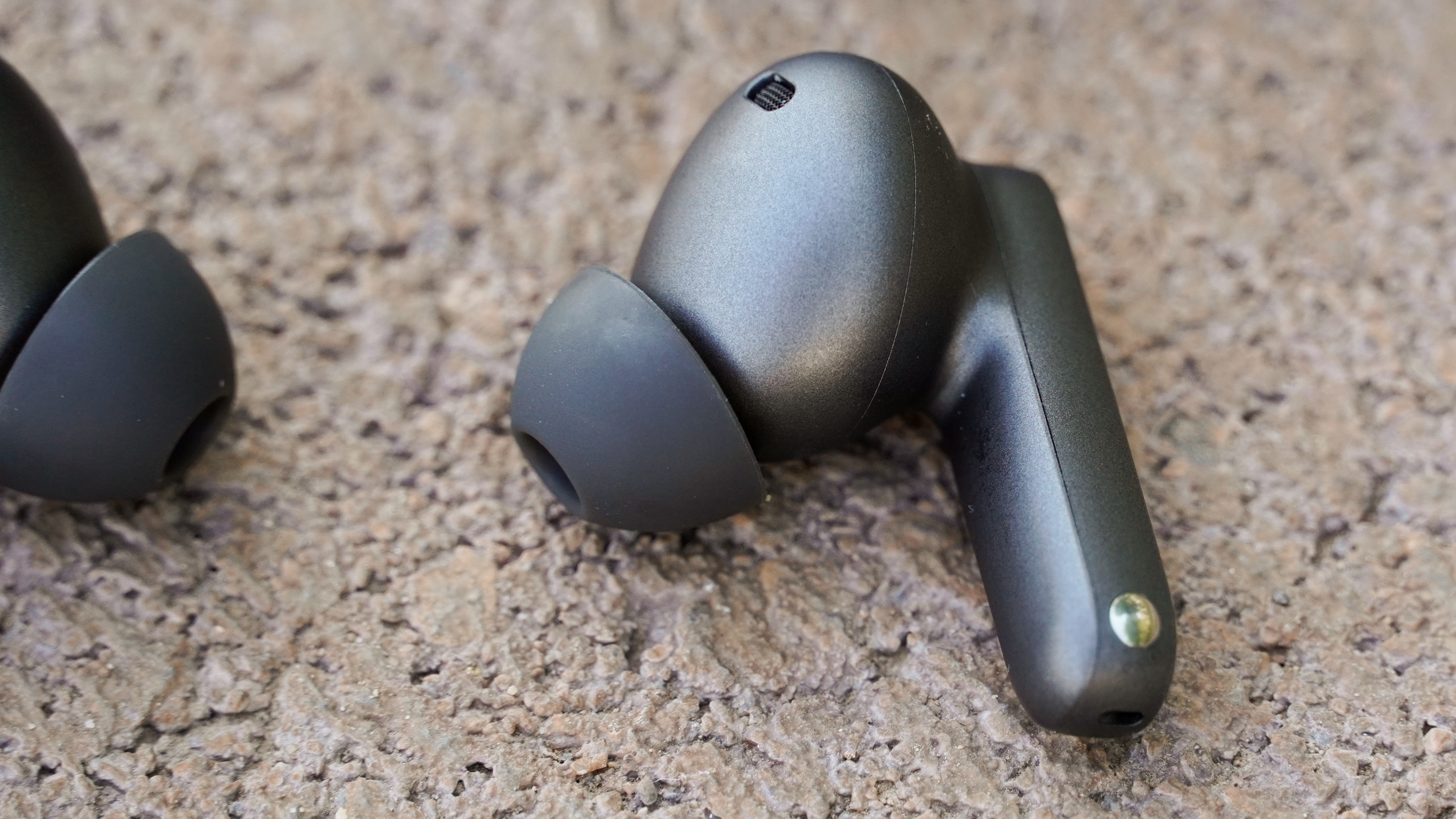 A OnePlus Buds 4 earbud on its side, showing the ear tip, vents, and charging contacts.