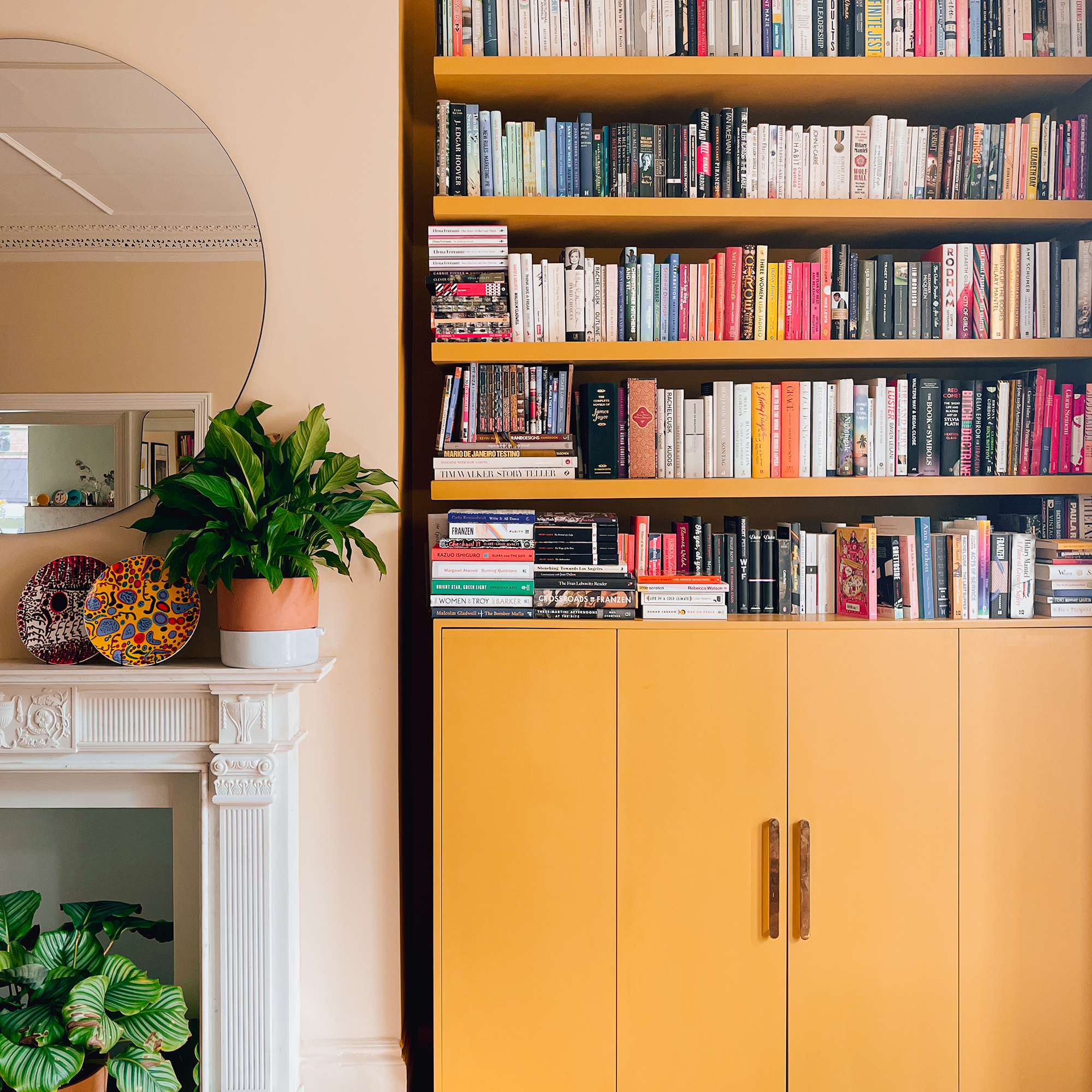 Yellow shelves filled with books with yellow cupboards below in the alcove of a soft pink living room