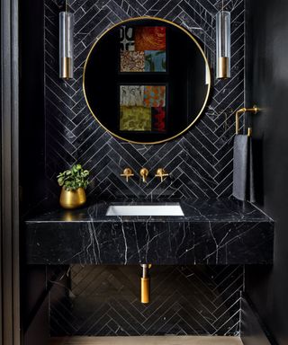 black bathroom ideas, black bathroom with herringbone tiled walls, black marble basin, brass figures, mirror, pair of matching pendant lights, wooden floor