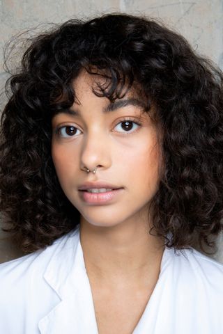 A model with a curly bob hairstyle and a white shirt.