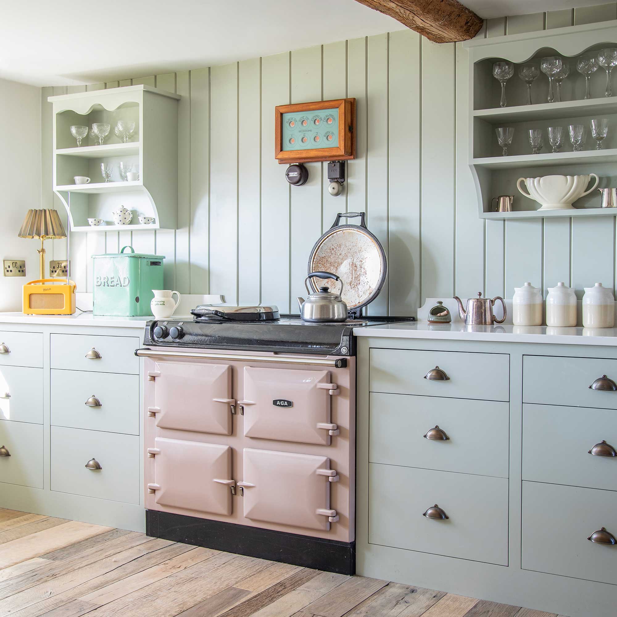 Green country kitchen with tongue and groove splashback, pink range cooker, open wall cabinets and vintage accessories
