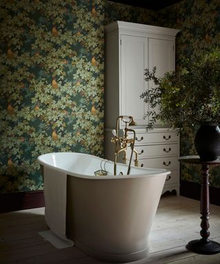 A green wallpapered bathroom with a white free standing tub with a green houseplant besides it