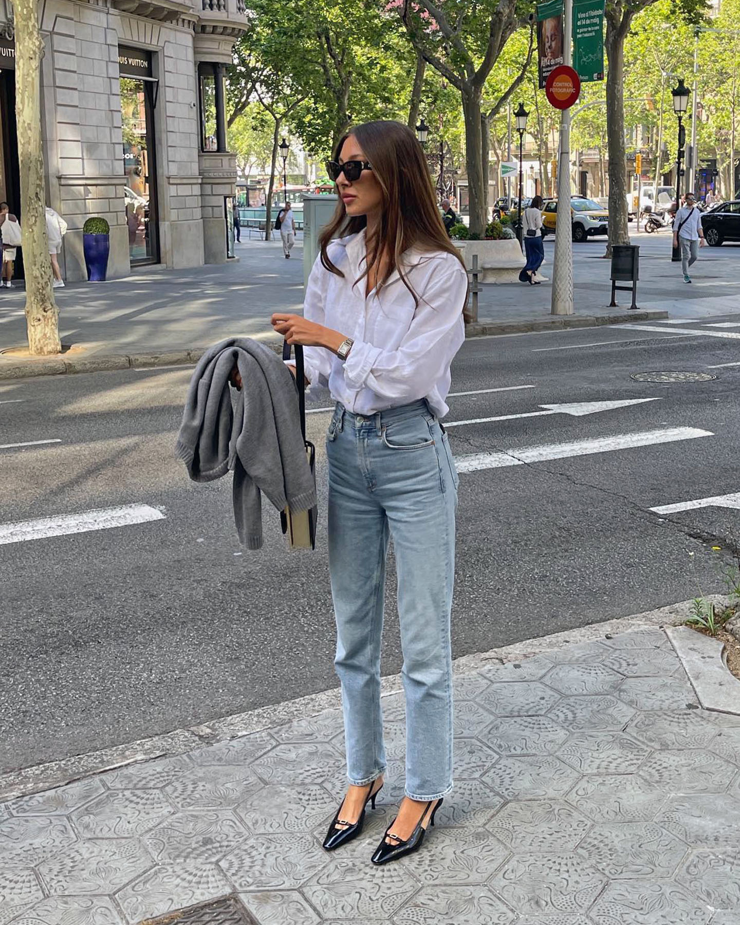 fashion influencer Felicia Akerstrom poses on the streets of Paris wearing a classic outfit with a white button-down shirt, straight-leg jeans, and black slingback heels