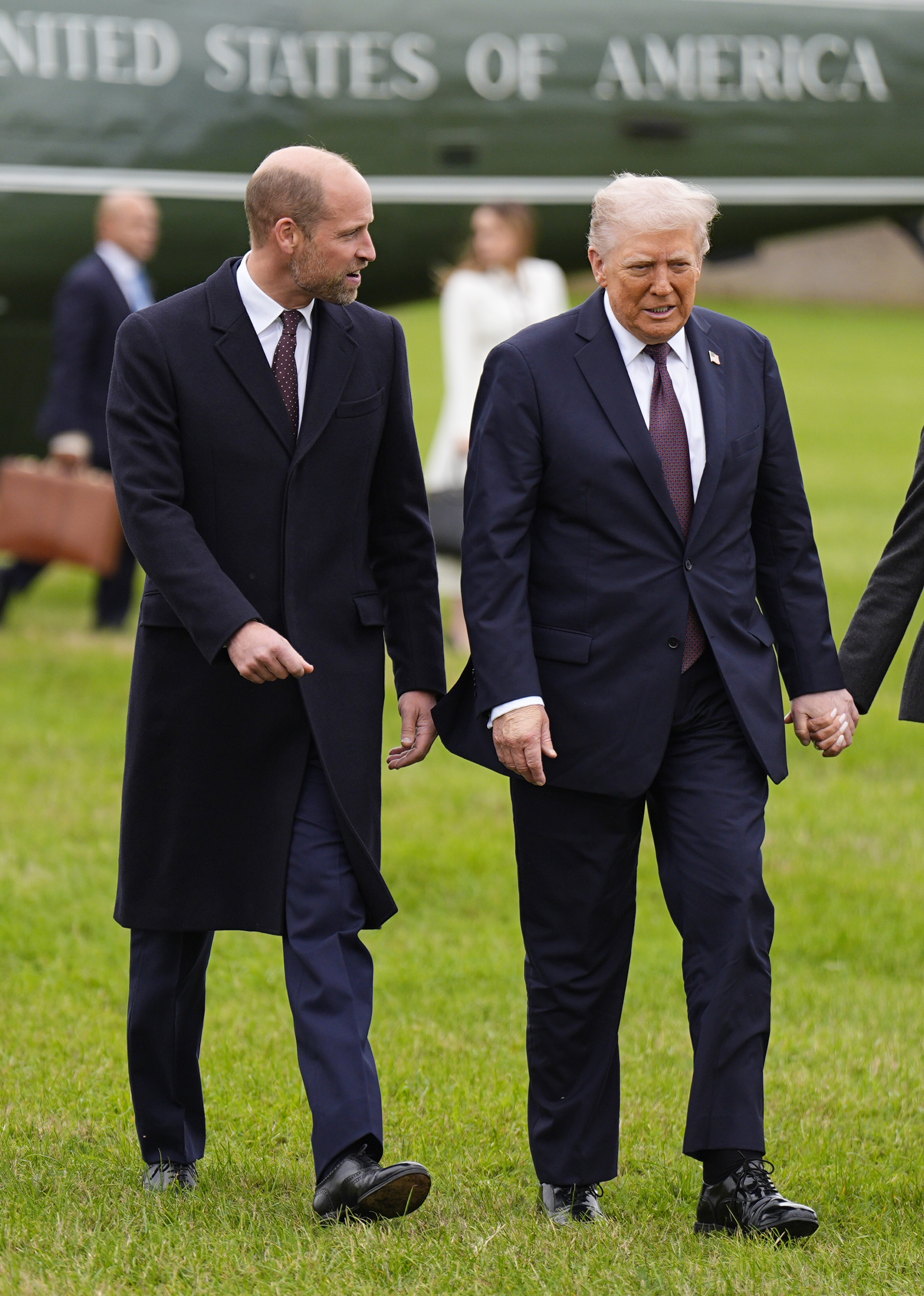 Prince William and Donald Trump walking across a field in front of a plane that says United States of America