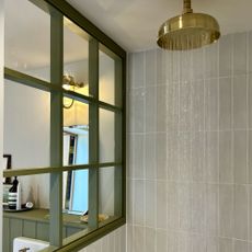 Water coming out of gold shower head in pale-green tiled shower enclosure
