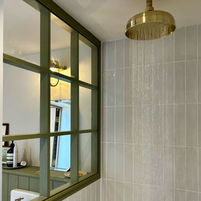Water coming out of gold shower head in pale-green tiled shower enclosure