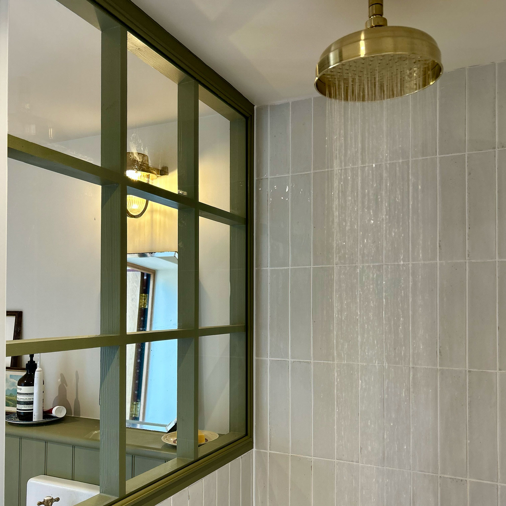Water coming out of gold shower head in pale-green tiled shower enclosure