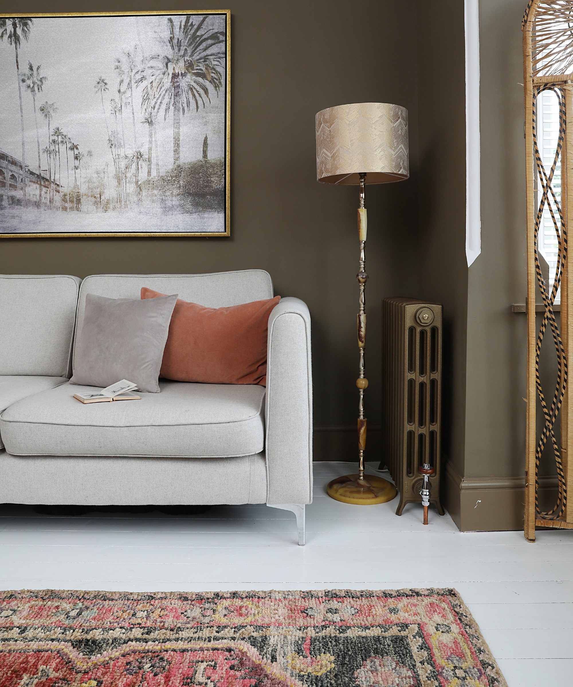 A living room with a grey sofa and brown walls, decorated with a vintage Moroccan rug and a golden floor lamp