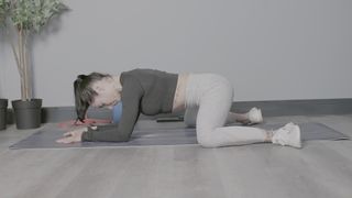 Frog pose demonstrated side on by writer Sam on yoga mat in studio