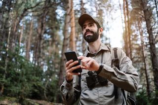 man using a smartphone and binoculars in a forest