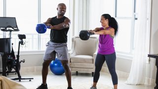 Couple working out at home doing kettlebell swings together