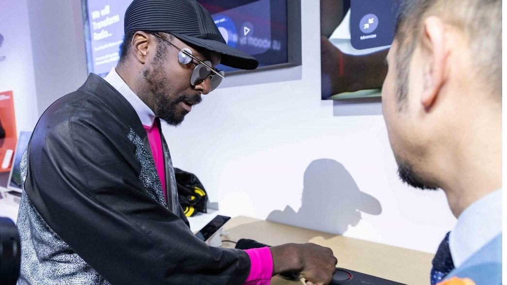 Will.i.am speaking about XBoom speakers at CES 2025, wearing all black with a black cap