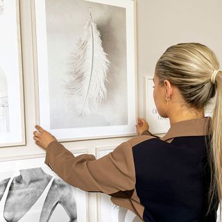 Molly Mae straightening a picture of a white feather on a cream wall photo gallery