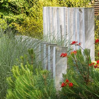 large timber uprights together with plenty of planting and red flowers to create natural privacy screening in a garden