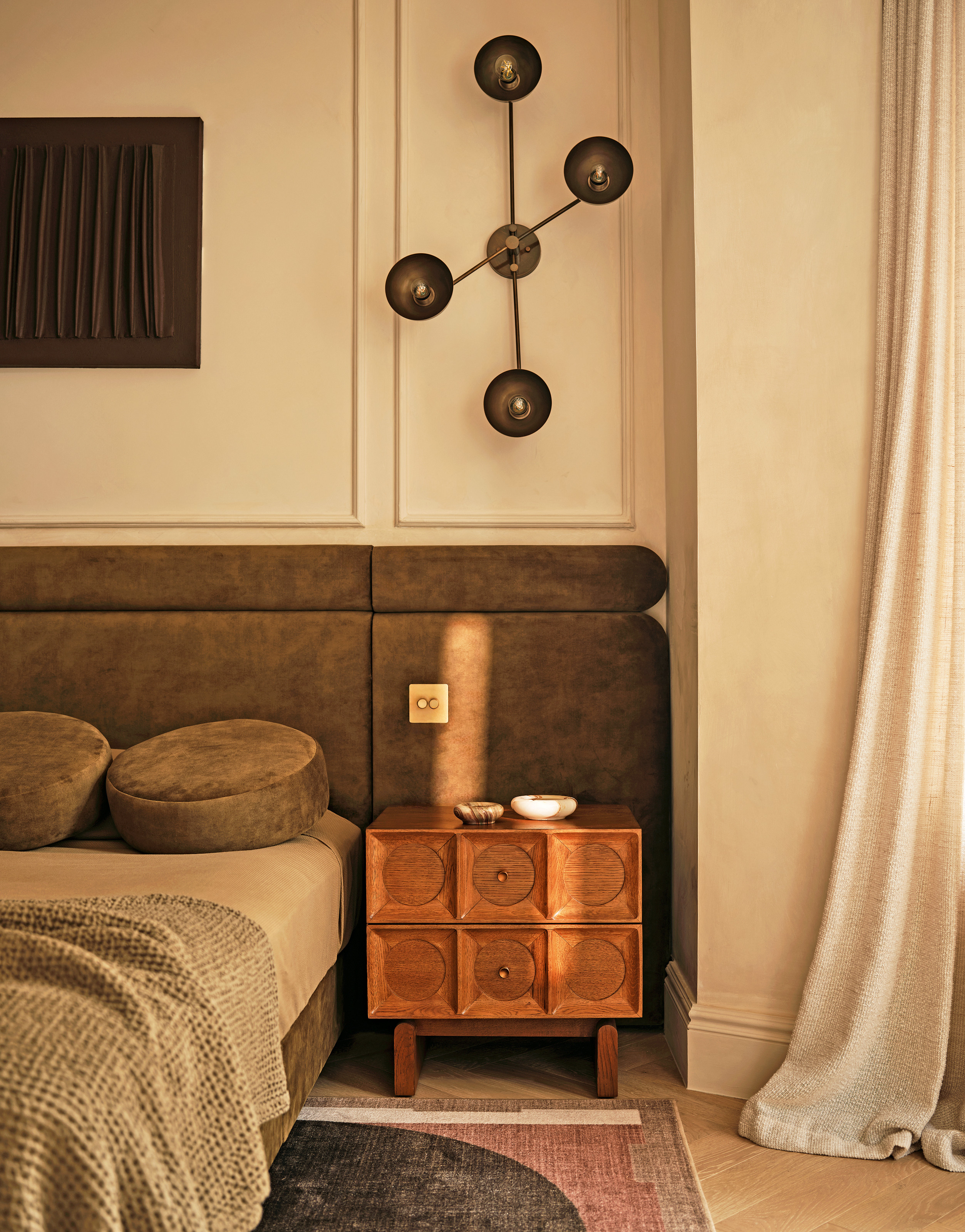 Bedroom with olive green upholstered extended headboard, wood side table, green bedlinen and round velvet cushions
