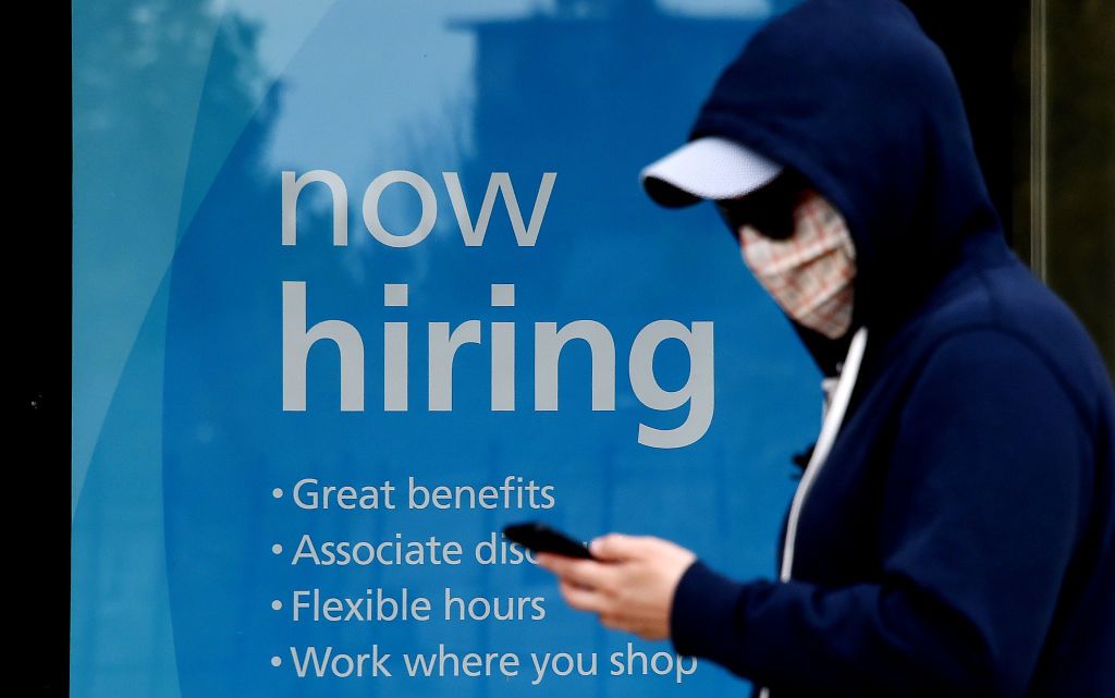 A man wearing a face mask walks past a sign &amp;quot;Now Hiring&amp;quot; in front of a store amid the coronavirus pandemic on May 14, 2020 in Arlington, Virginia