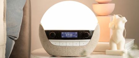 The Lumie Bodyclock Luxe 700FM sunrise alarm on a warmly-lit bedside table. 