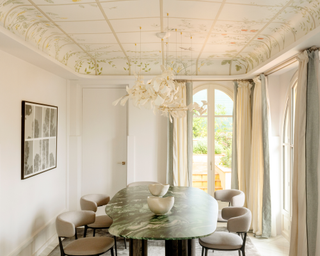 Cream colored dining area with decorative ceiling elevated by feminin sculptural pendant above modern curved table