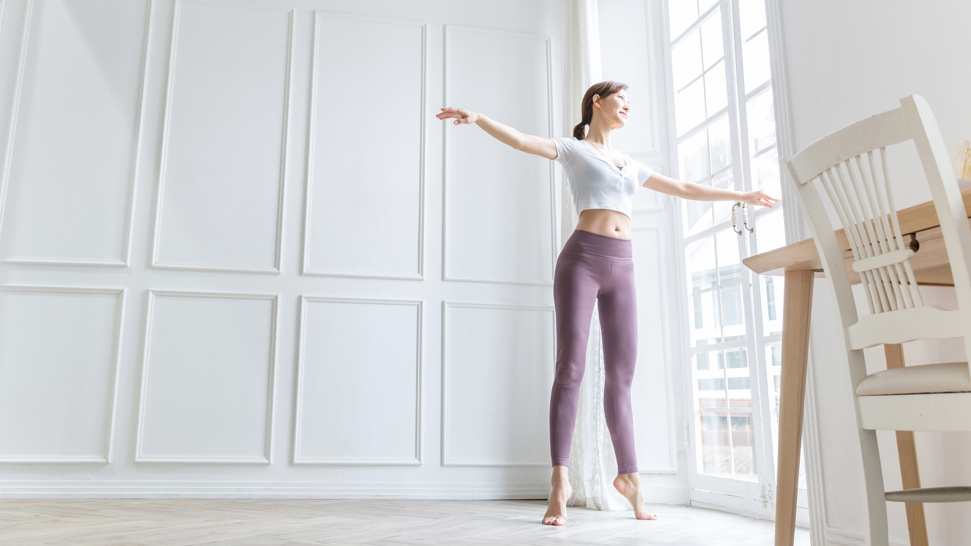 Woman standing by window on her toes