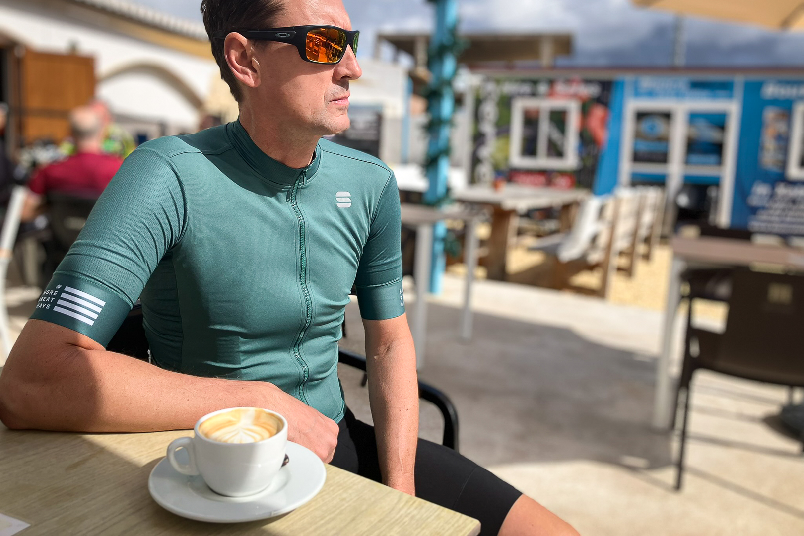 Man sitting at a cafe drinking a coffee wearing a green cycling jersey
