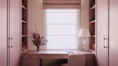 color-drenched pink home office with sheer blinds, cabinets on either side, vase of flowers, glass table lamp, and pink built-ins