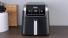 Ninja Air Fryer Pro XL on a gray counter with white pot of black utensils and a wooden chopping board leant against light gray wall
