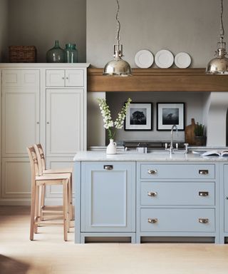 a country-style pale blue kitchen with white cabinets, and a huge island with a marble top and blue cabinets