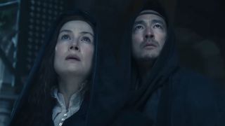 A hooded Moiraine and Lan looking up at the off-camera White Tower in The Wheel of Time season 3