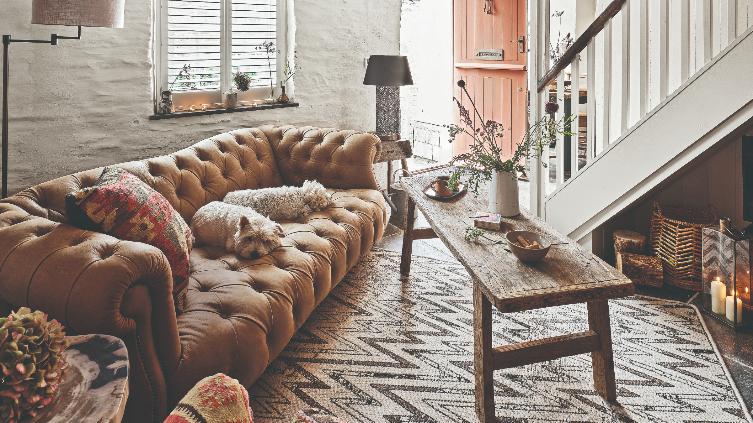 A rustic white-painted living room with a brown leather Chesterfield sofa and a wooden coffee table