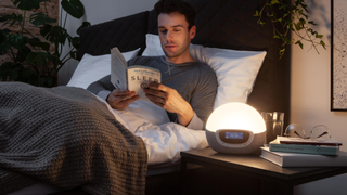 A man reading a book in bed, lit by the Lumie Bodyclock Shine 300 in a warm light