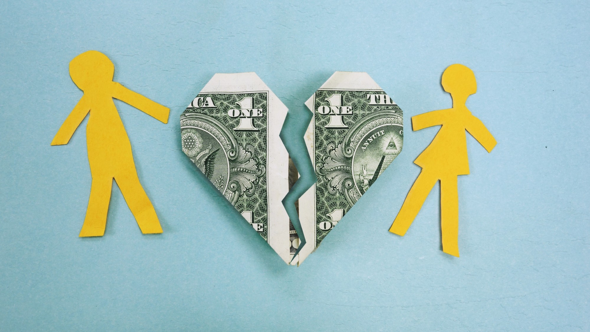 Paper doll cut-out couple with a broken heart made out of a dollar bill between them