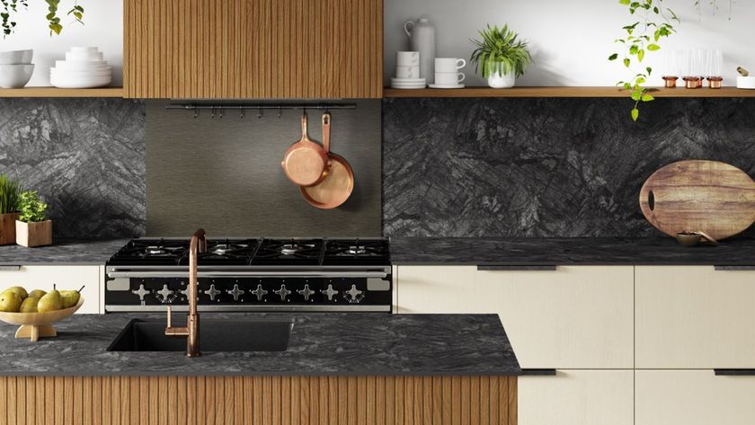 Modern kitchen with dark stone-effect worktops, vertical timber cabinetry and cream base units. A black range cooker sits against a dramatic charcoal splashback, with copper pans hanging above and a black inset sink with a copper tap in the island.
