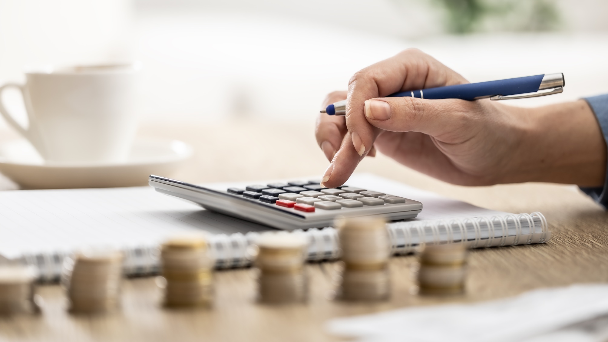 A woman uses a calculator next to stacks of coins of various heights.