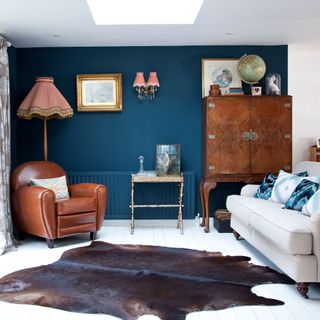 a living room with blue walls and white floor, with a brown cowhide rug, brown leather armchair and white couch