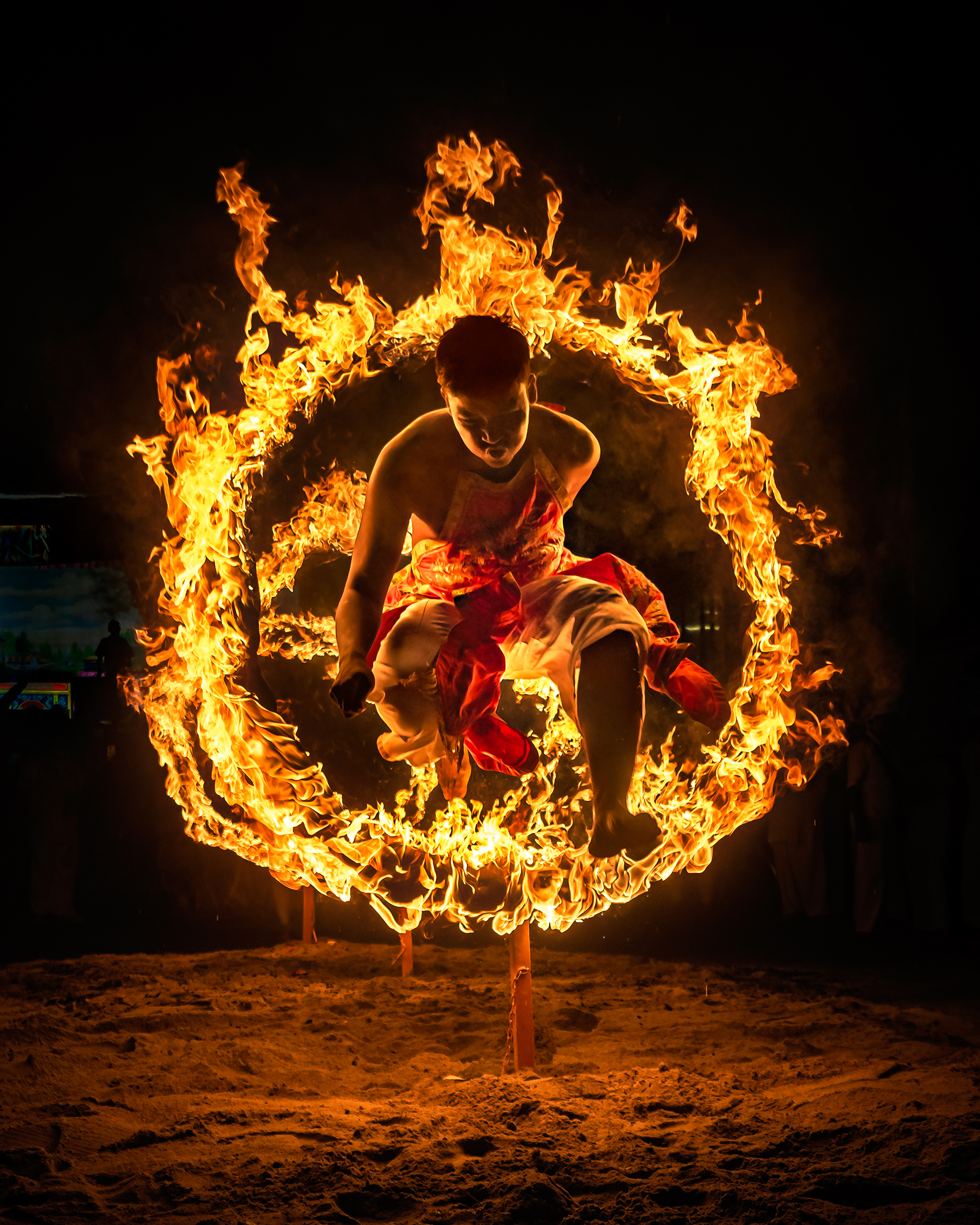 A performer leaps through a fiery ring, showcasing fire dancing skills against a dark background. Flames illuminate the scene dramatically