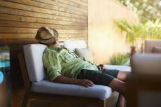 A middle-aged man sleeps outside with a hat over his face.
