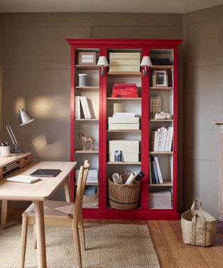 stone home office with red shelving unit, rug, desk, baskets, wooden floor