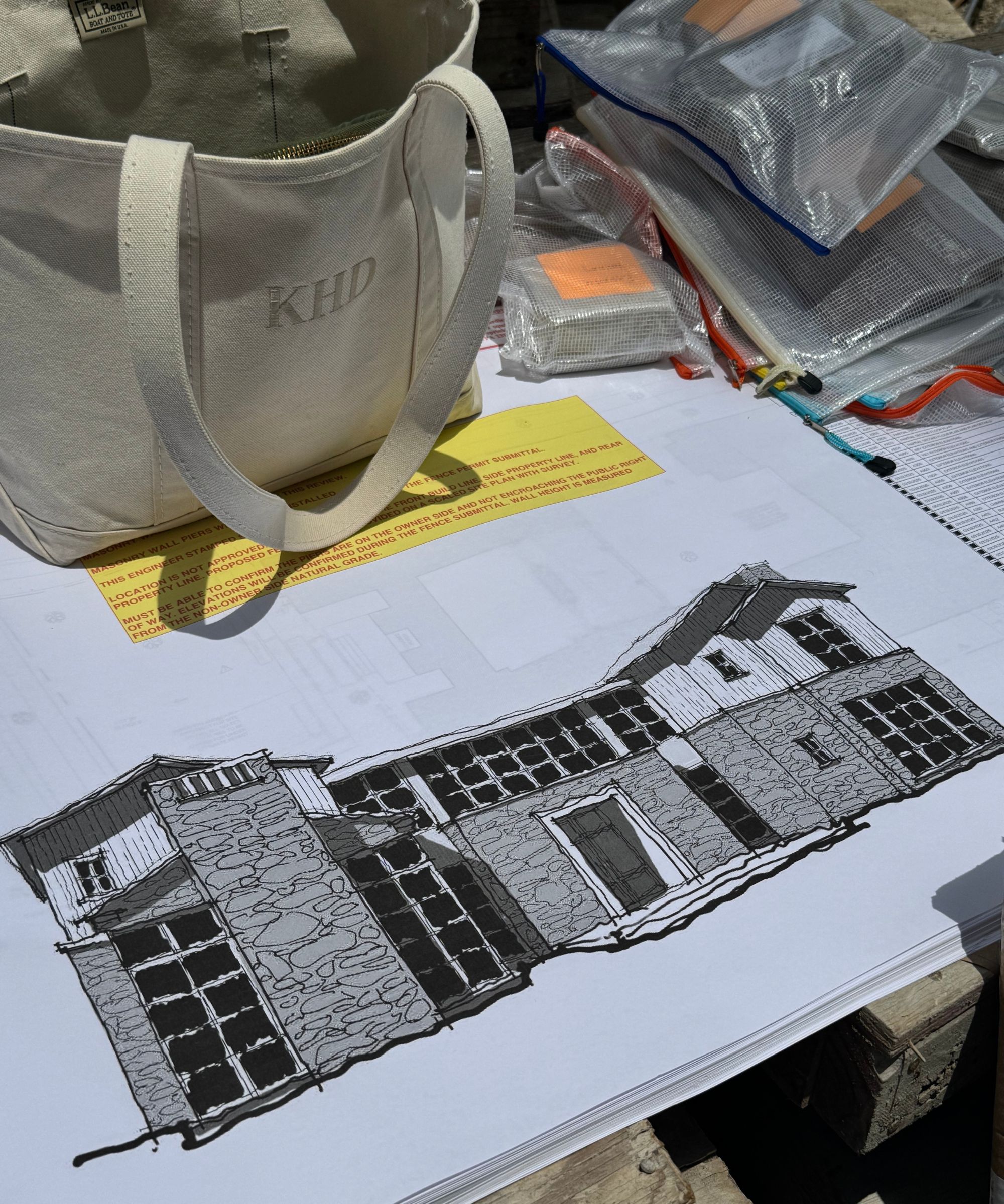 Close up of drawing of the front of a house in black and white, other papers and handbag on table