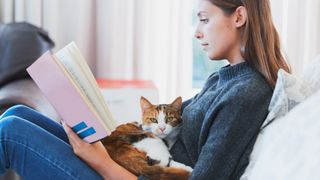 Woman reading book with cat on her lap
