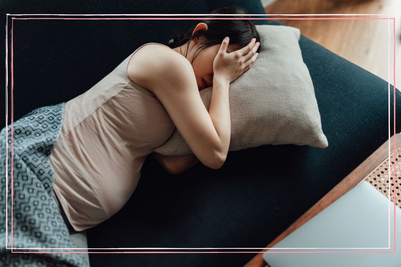 A pregnant woman lying on a sofa and covering her face with her hand