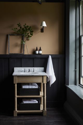 yellow ochre bathroom with marble topped vanity, black panelling, wall light, green painted window, dark wooden floors