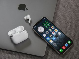 An iPhone sat next to an Apple Mac and a pair of Airpods