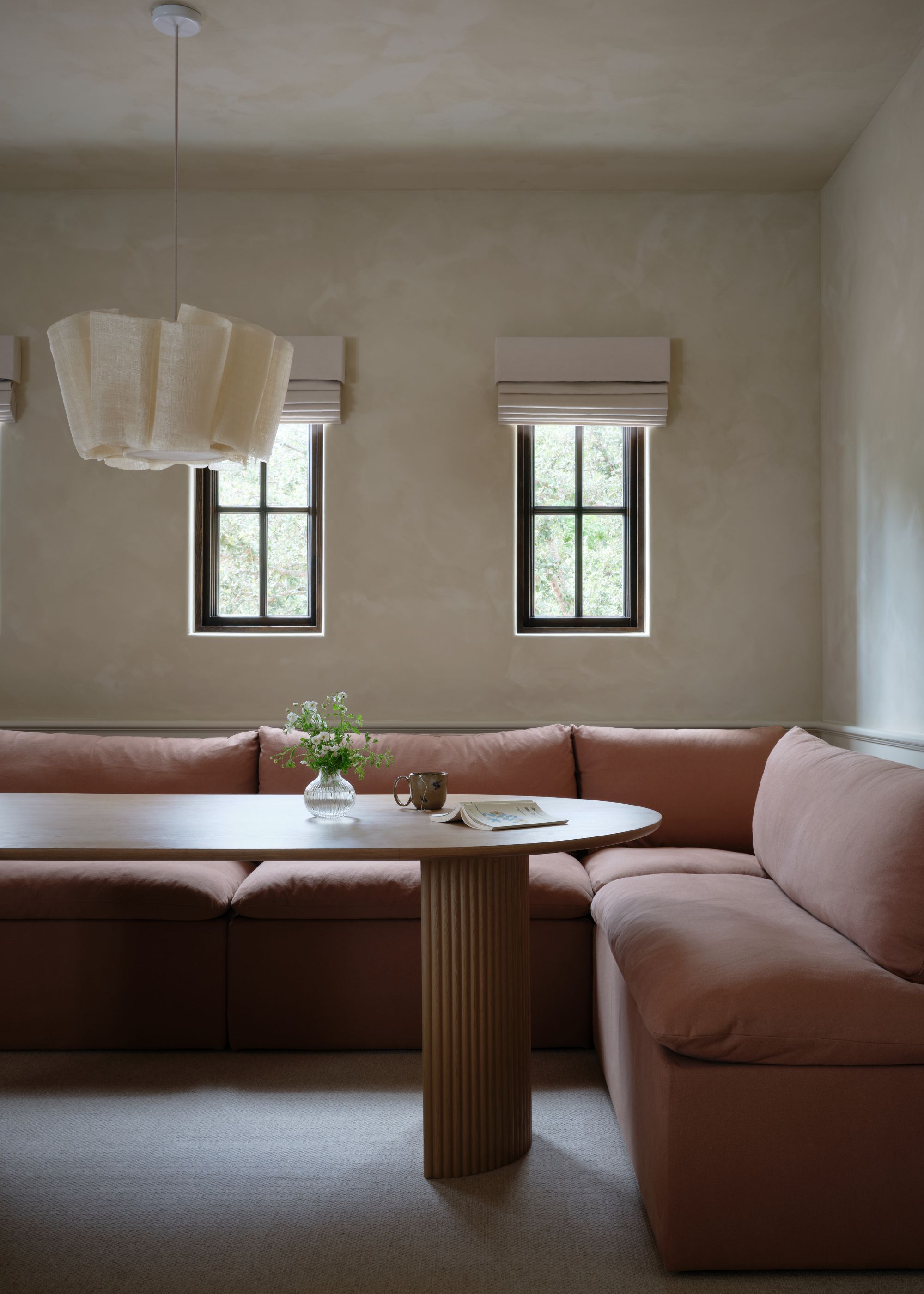 A dining nook with limewash walls, banquette corner seating in a plush terracotta, and a modern wooden dining table with a minimalist form.