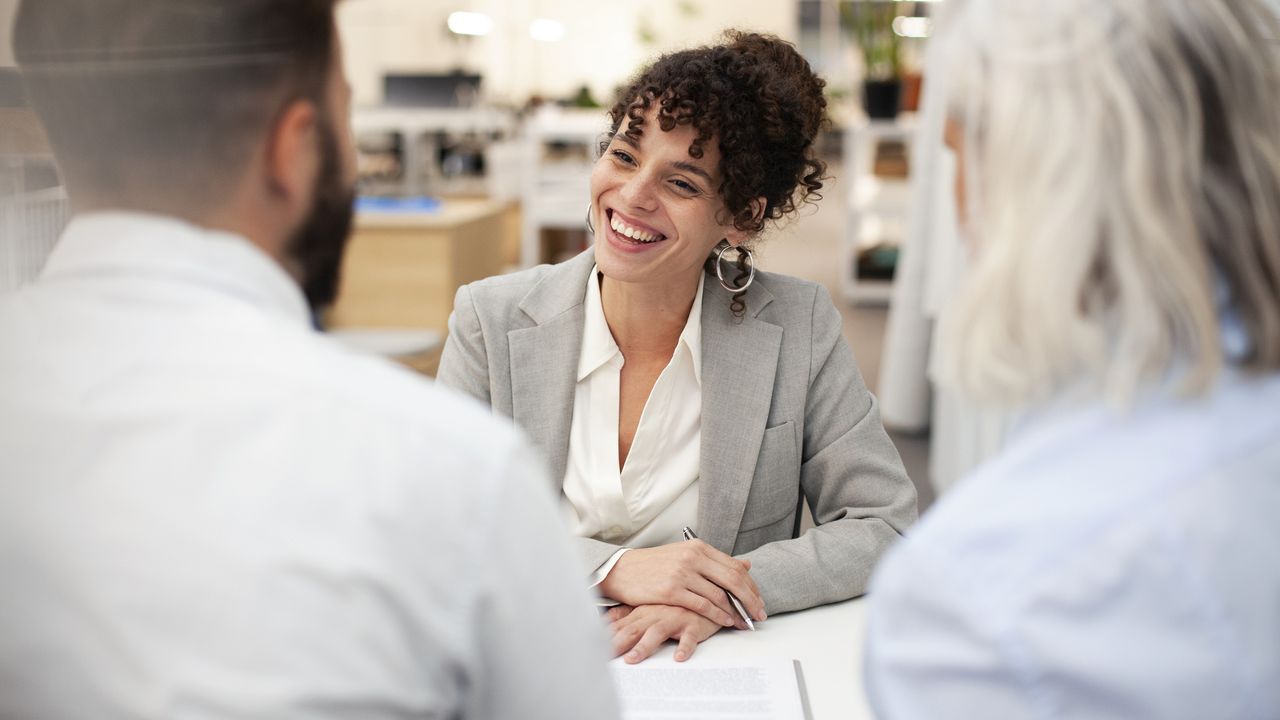 A financial adviser smiles as she speaks with two clients.