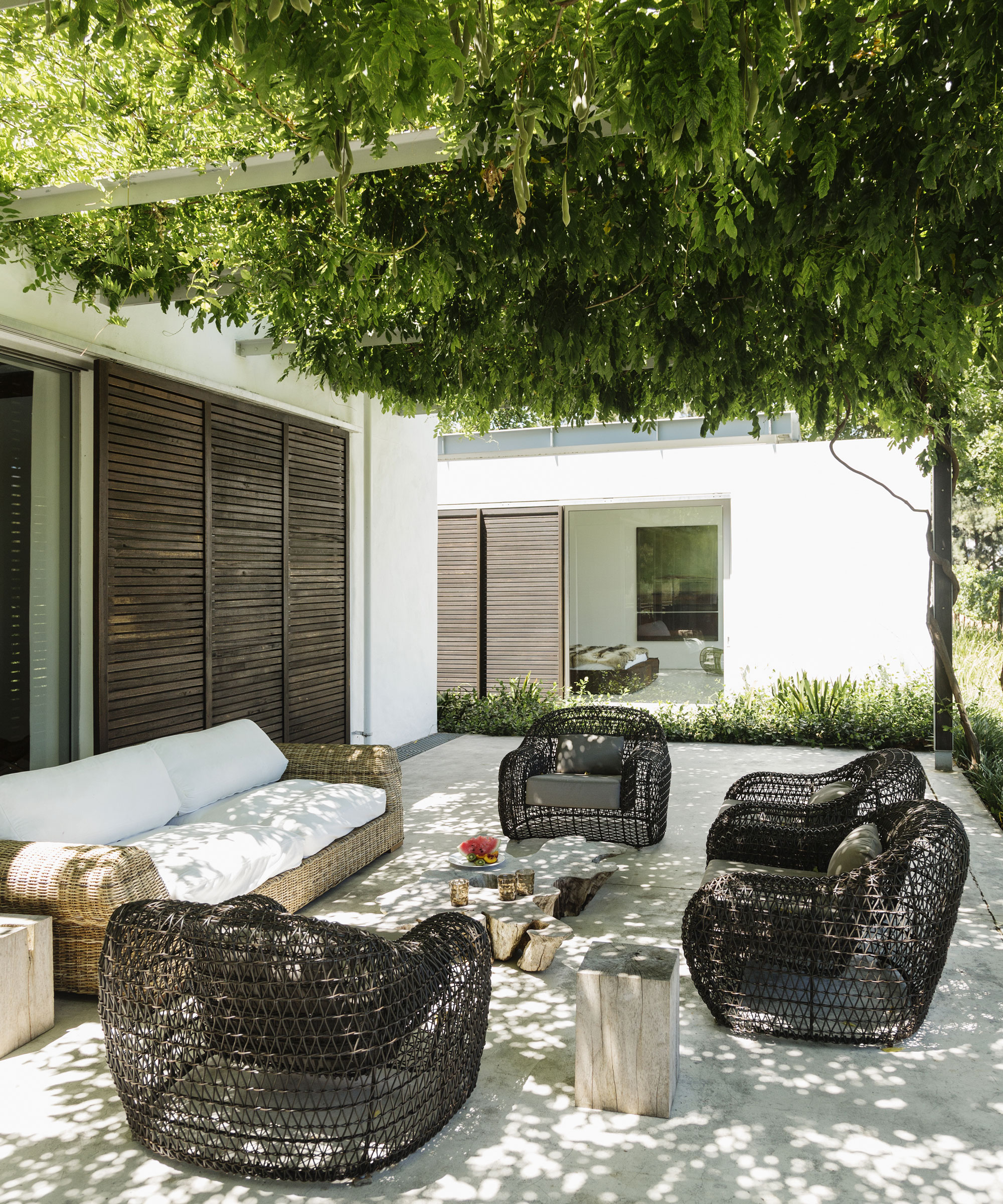 patio area with sofa, chairs and table, with a pergola covered in climbing plants, and doors to house