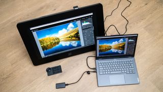 XPPen Artist Pro 24 (Gen 2) 4K drawing tablet next to a laptop with wires trailing from it on a wooden surface