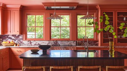 A large color drenched terracotta kitchen with a fluted wood island and marble countersplash