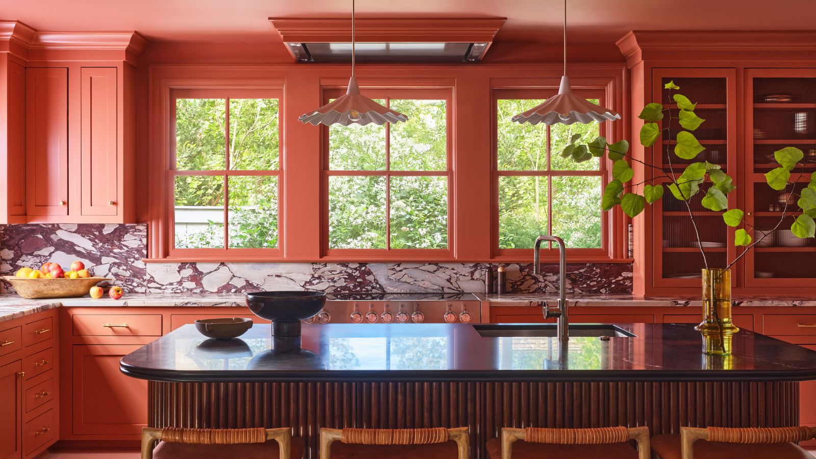 A large color drenched terracotta kitchen with a fluted wood island and marble countersplash