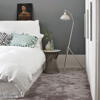 Grey carpet in bedroom, bedside table, floor lamp, white bedding and striped cushions